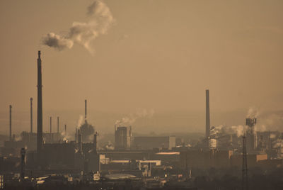 Smoke emitting from factory against sky at sunset