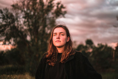 Portrait of beautiful young woman standing against trees