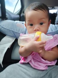 Portrait of cute baby girl holding milk bottle while sitting in car