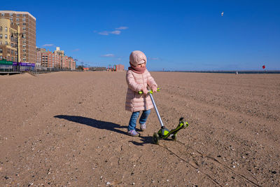 Little girl in a bubble coat dragging her scooter through the sand
