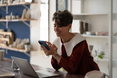 Happy successful woman small business owner chatting on mobile phone while working in pottery shop