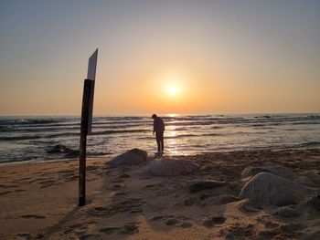 Man standing on beach against sky during sunset