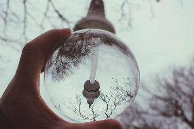 Cropped image of person holding glass ball with upside down reflection