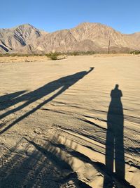 Shadow of person on sand in desert against sky