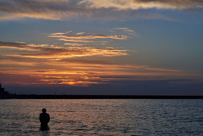 Silhouette man looking at sea against sky during sunset