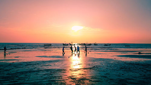 People playing at beach during sunset