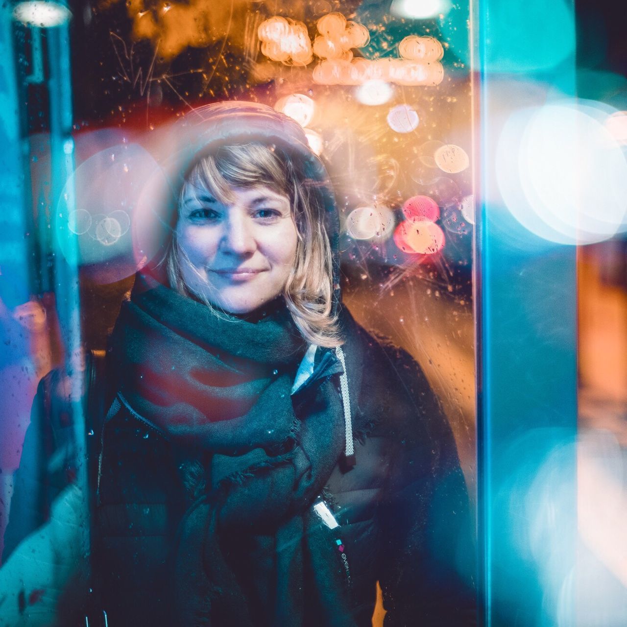 PORTRAIT OF A SMILING YOUNG WOMAN STANDING AGAINST ILLUMINATED LIGHT