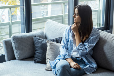 Young woman using phone while sitting on sofa at home