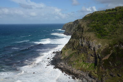 Scenic view of sea by rocky mountains against cloudy sky