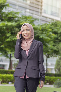 Happy businesswoman using smart phone while standing against office building