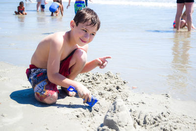 Full length of shirtless smiling boy playing at sandy beach