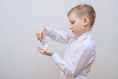 Boy looking away while standing against white wall