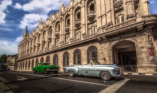 Cars on road by building in city against sky