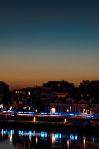 Illuminated buildings by river against clear sky at night