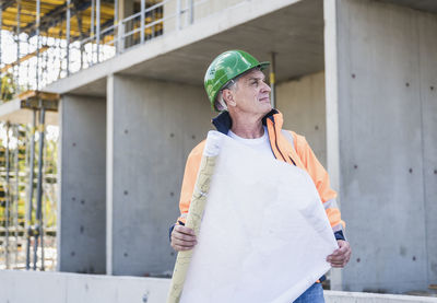 Thoughtful contractor with plan standing at construction site