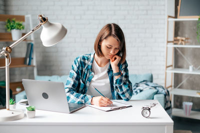 Young woman using mobile phone while sitting on table