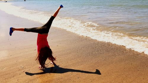 Full length of girl doing handstand on shore at beach during sunny day