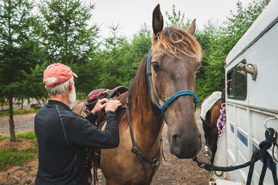 Man tying saddle on horse by van