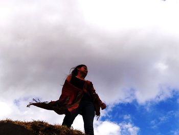 Low angle view of woman standing on cliff against cloudy sky