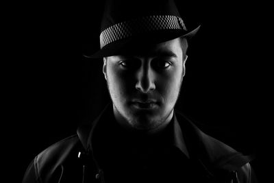 Close-up portrait of young man wearing hat over black background