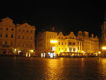 Illuminated buildings by street against sky at night