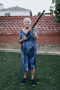 Full length of man holding umbrella standing against brick wall