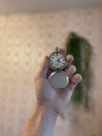 Close-up of hand holding clock against blurred background