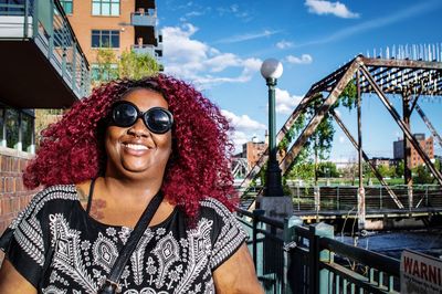 Redhead smiling woman standing by railing against sky