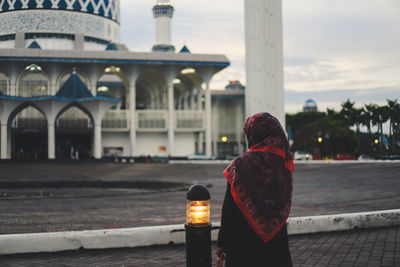 Rear view of young woman standing outside mosque against clear sky