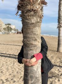 Midsection of woman standing on tree trunk at beach against sky