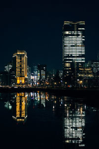 Illuminated buildings by river against sky at night