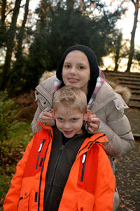 Portrait of happy girl pulling ears of brother standing in warm clothing at park