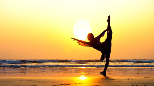 Silhouette woman practicing yoga at beach against clear sky during sunset