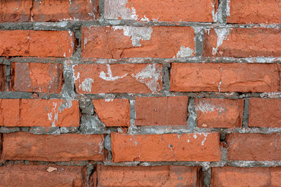 Full frame shot of red brick wall with damaged grey layer of plaster