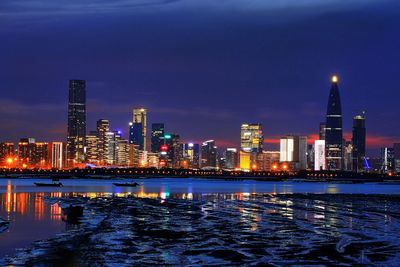 Illuminated buildings by river against sky at night