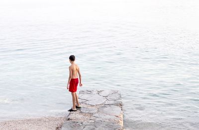 Rear view of shirtless teenage boy standing on pier at beach