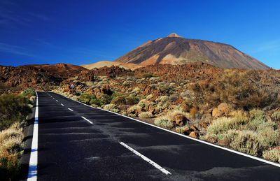 Empty road along rocky landscape against blue sky