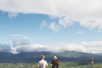 Rear view of tourists standing against mountain landscape and sky