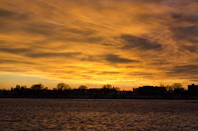 Scenic view of lake against dramatic sky during sunset