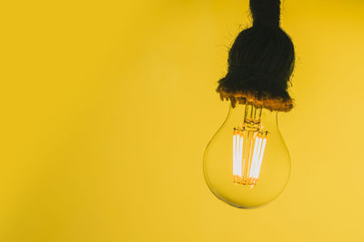 Close-up of light bulb hanging against yellow background