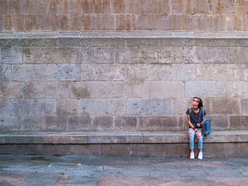 Full length of teenage girl sitting against wall