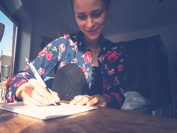 Young woman writing on book at table