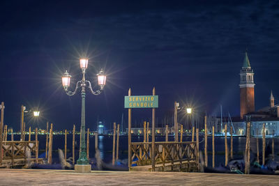 Illuminated street lights by sea against sky at night