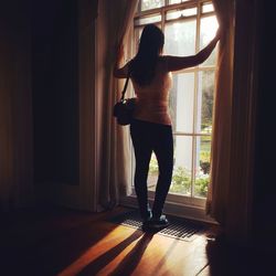 Rear view of woman standing by window at home