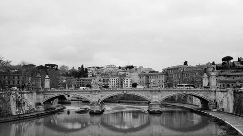 Bridge over river by buildings against sky