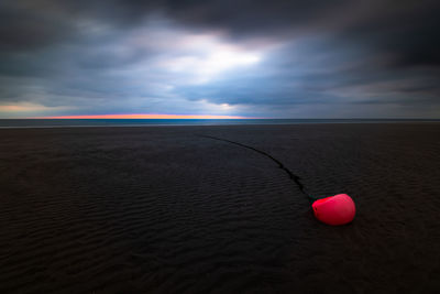 Orange buoy at beach of amrum island during low tide with dramatic sky and dark clouds at sunset