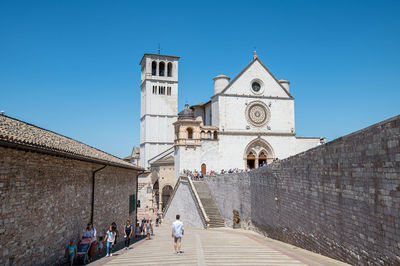 People at historic building against clear blue sky