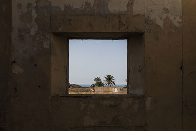 Window frame of old building against sky with view of palm trees in el chorrillo, almeria, spain