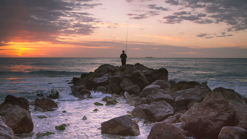 Man standing on rock at beach during sunset