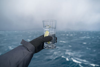 Hand holding glass of water against sky